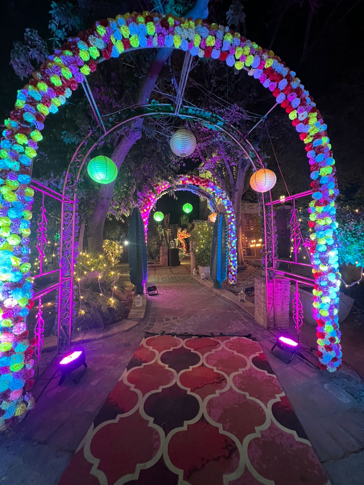 Floral tunnel walkway with patterned crimson runner carpet and ambient uplighting